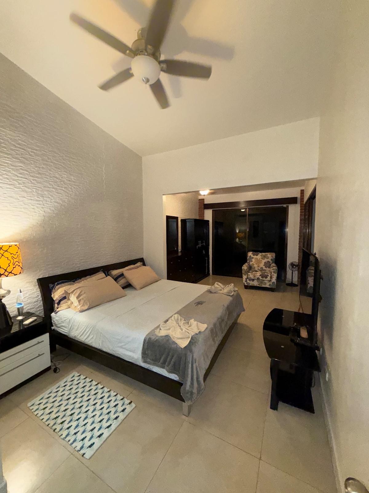 Primary bedroom with a king bed, ceiling fan, and a small sitting area